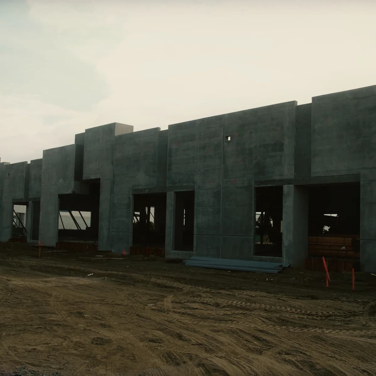 Concrete walls standing and braced to form the shell of a building, with openings formed in each panel