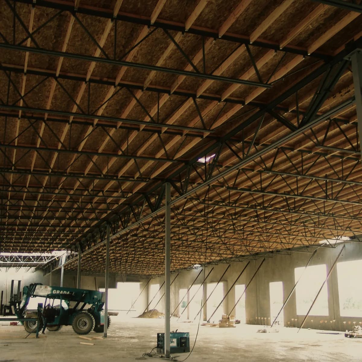A timber and steel roof structure spanning the inside of a completed building shell, seen from the floor