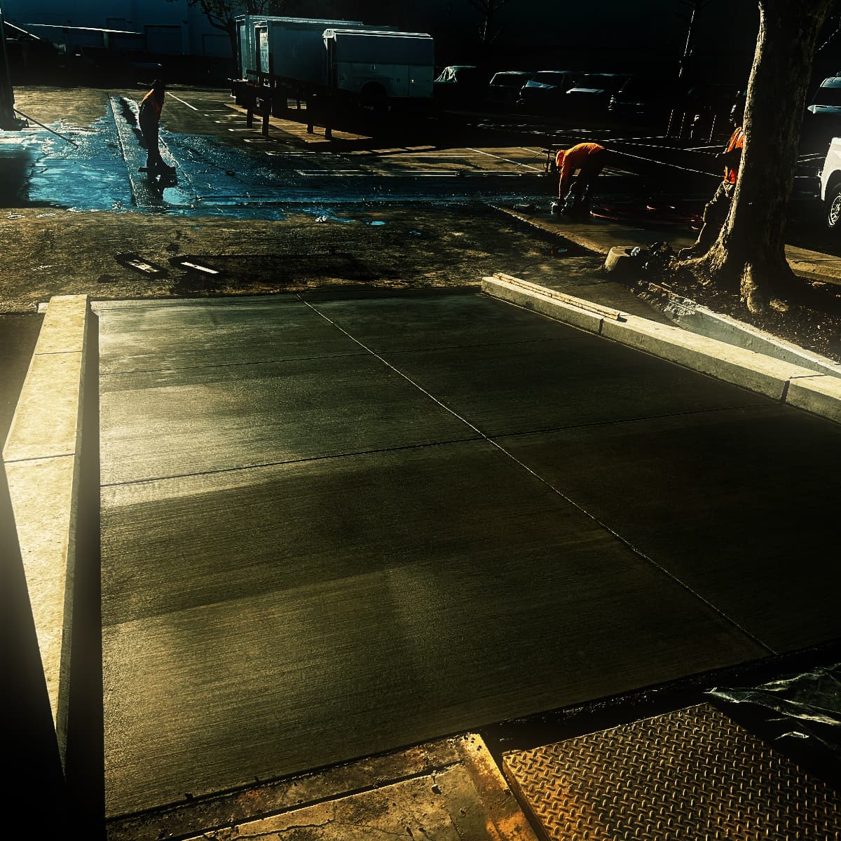 A completed commercial apron divided into panels by tooled control joints, raking light across its broom-textured surface