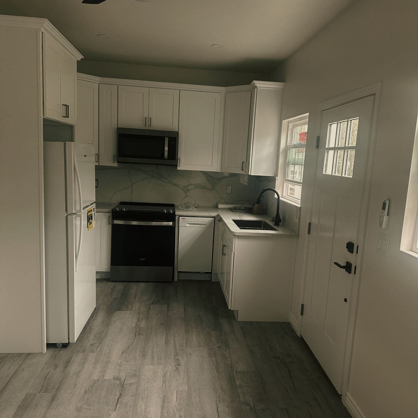 The finished kitchen of the Newbury Park accessory dwelling unit, with white shaker cabinetry, a quartz counter and full-height backsplash, and stainless appliances