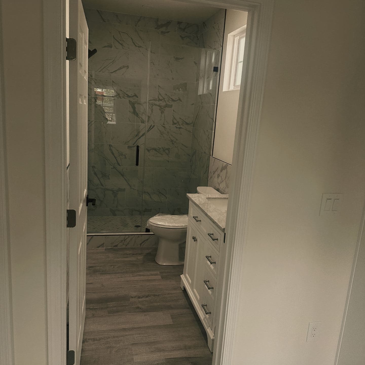 The bathroom of the Newbury Park unit, tiled full height with a frameless glass shower enclosure, matte black fittings and a skylight above