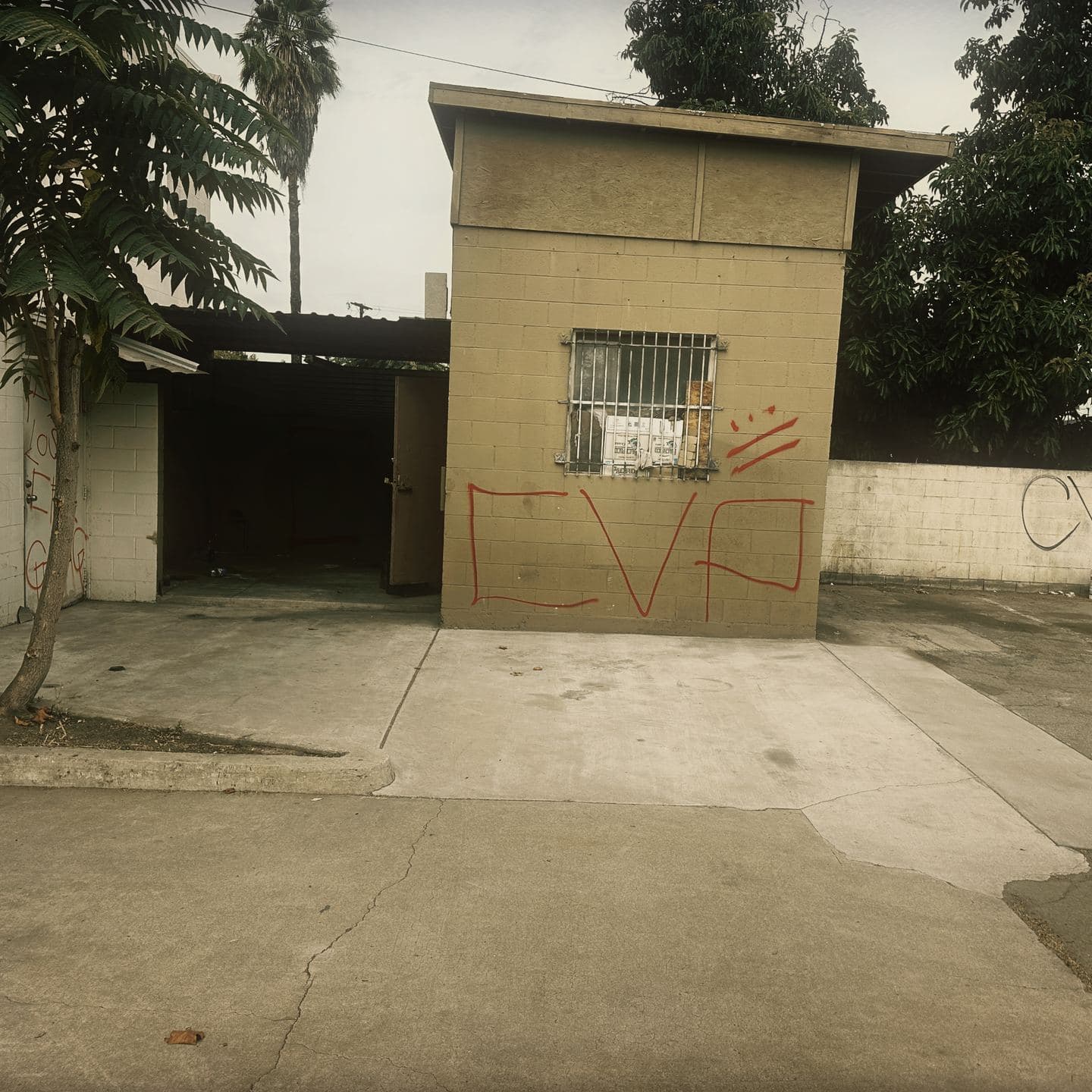 A detached masonry kiosk and open carport at the rear of the Pomona site, tagged in red, with cracked concrete across the yard