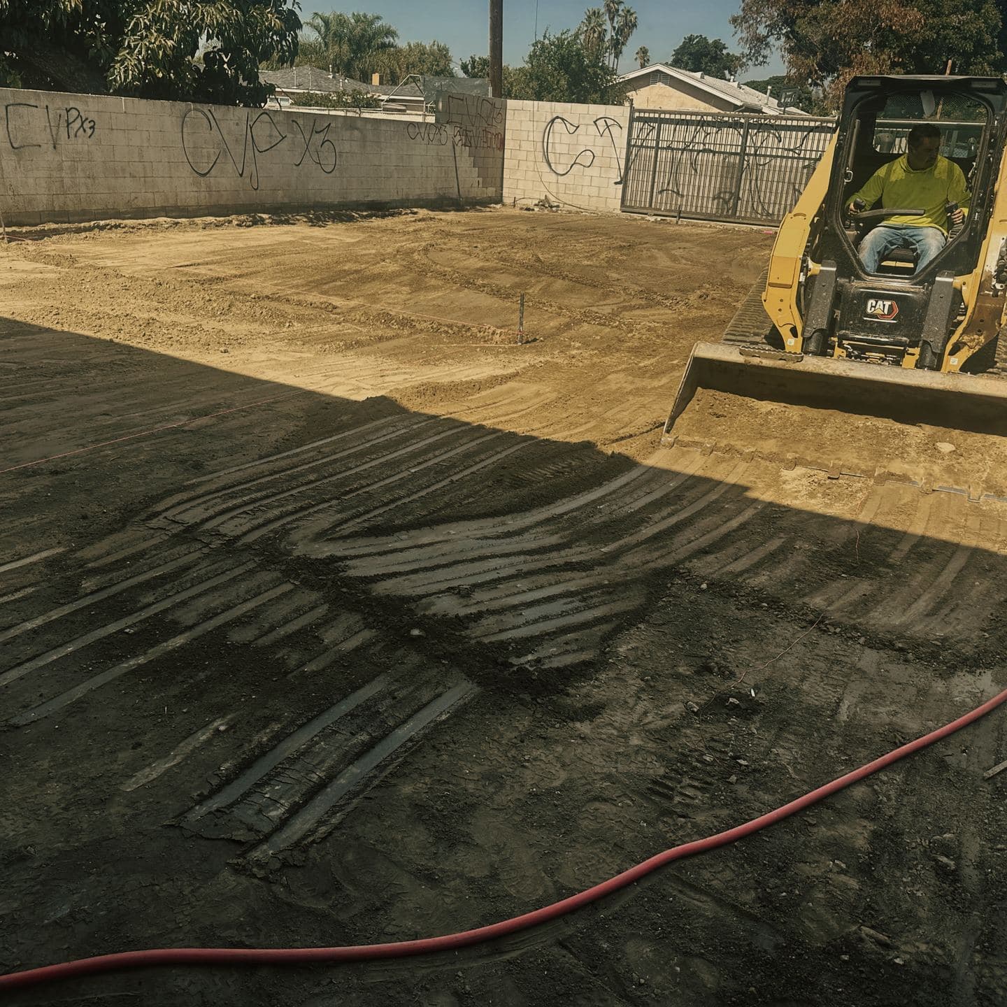 The Pomona lot graded and tracked flat, a compact track loader working at its edge against the boundary wall