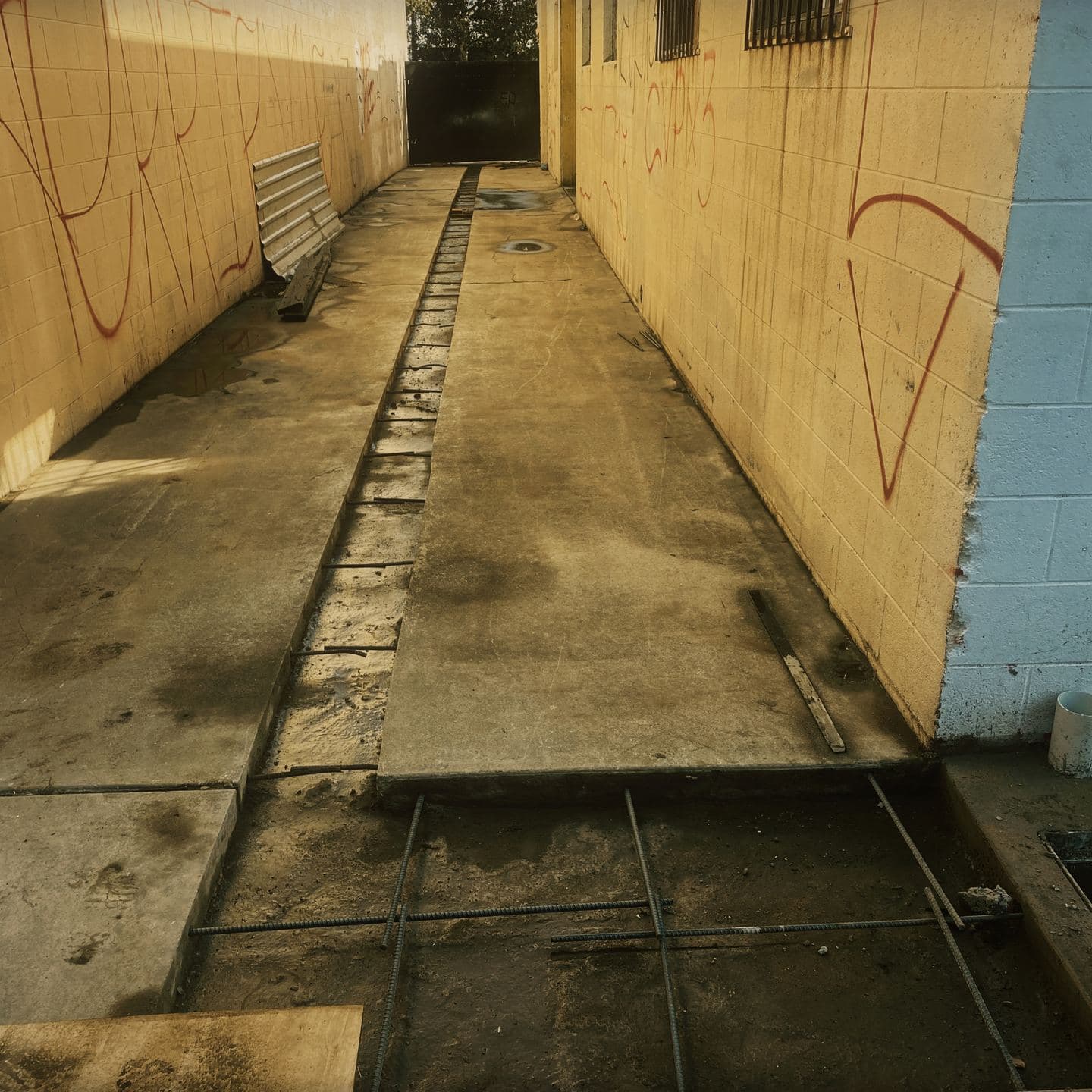 A linear trench drain running the full length of newly placed concrete along the side elevation in Pomona, with a reinforcement mat and catch basin set in the next section