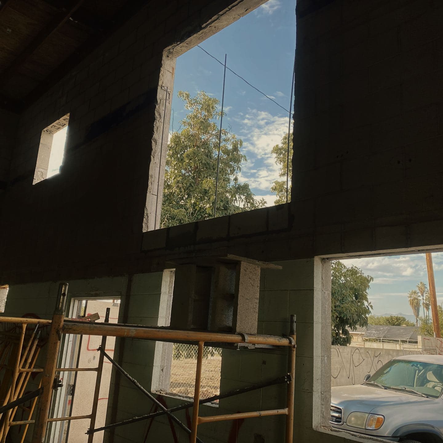 New openings cut through the existing concrete block shell in Pomona, seen from inside with the original roof joists above and scaffold in the foreground