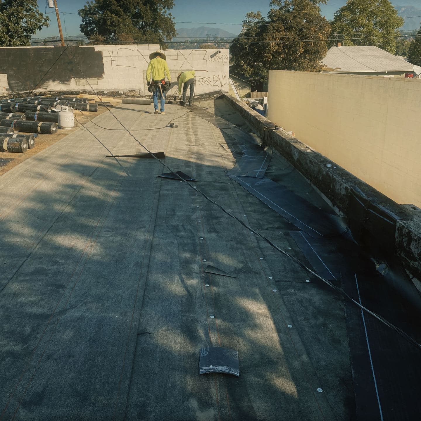Rolled roofing membrane being laid across the flat roof in Pomona, with unopened rolls stacked across the deck behind