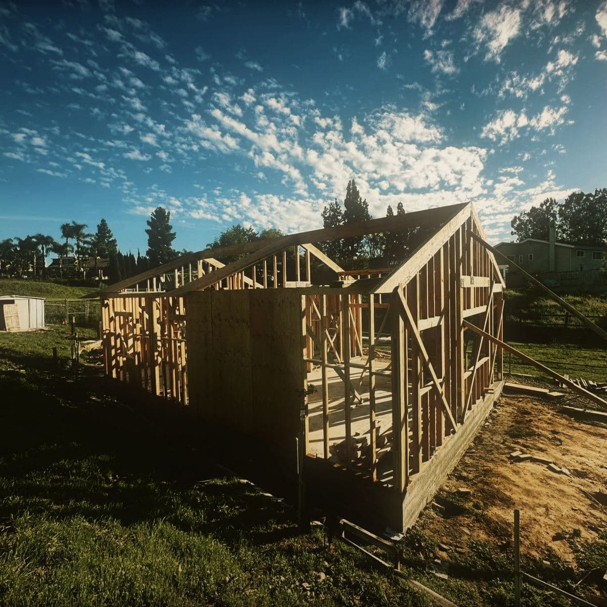 The timber frame of the guest house standing on its slab, wall studs and rafters up and the gable end taking shape