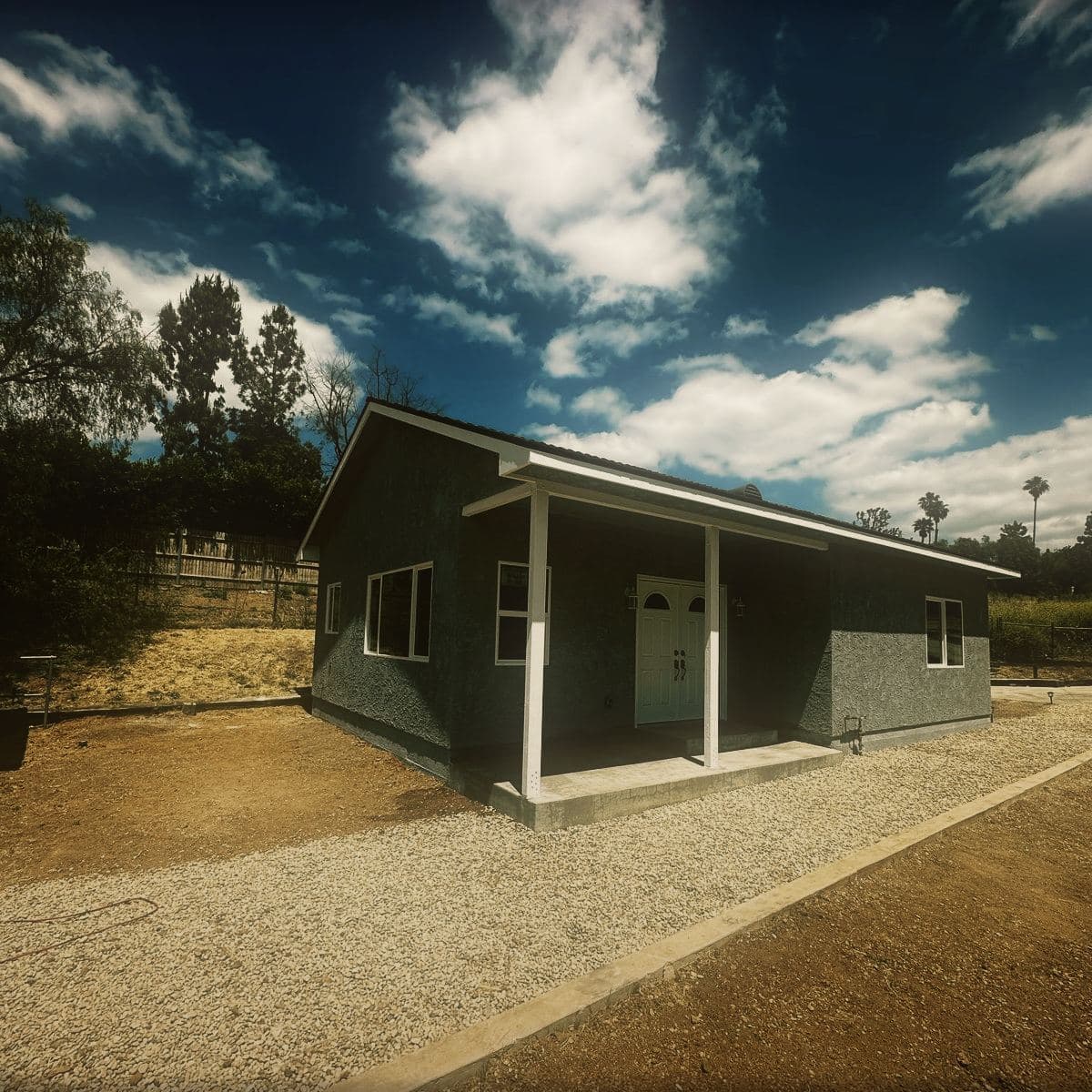 The finished guest house from the front, its covered porch, gable end and painted siding complete above a gravel apron