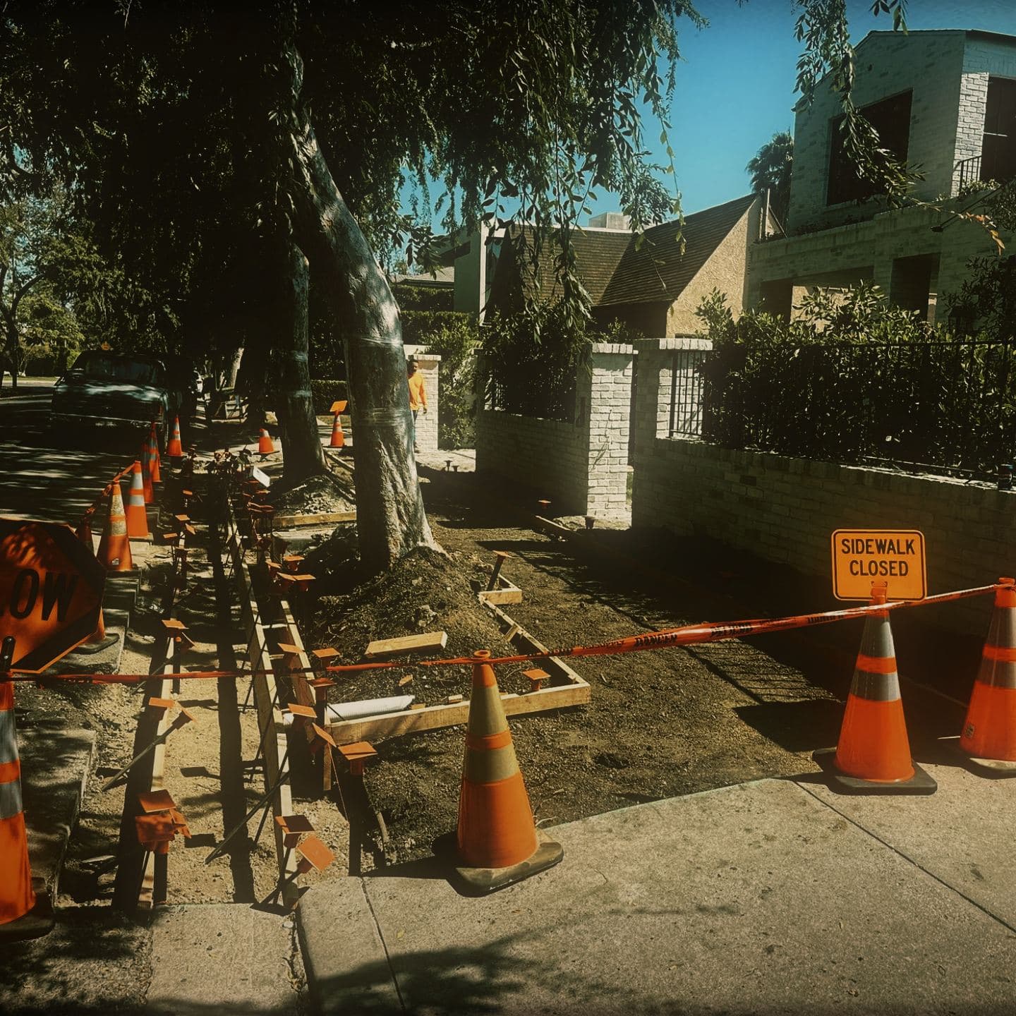 A SLOW paddle and a SIDEWALK CLOSED sign set against a cone taper and red barrier tape alongside the formed right-of-way at Westmount