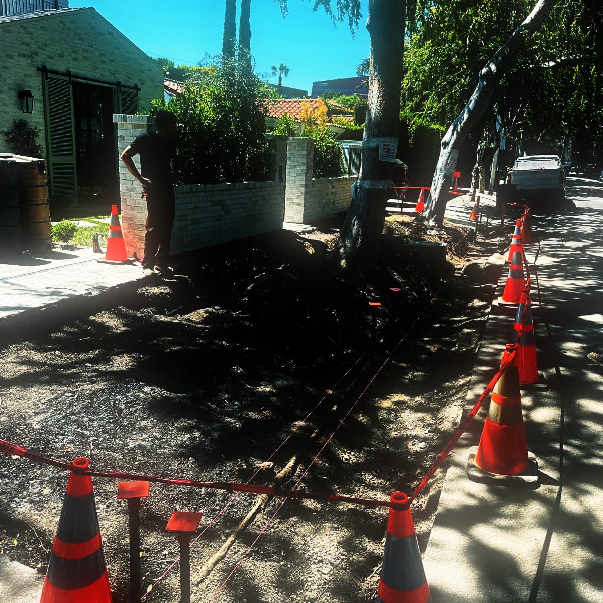 A frontage stripped back to subgrade with a stringline run on capped stakes down its full length, cones and barrier tape holding the closure