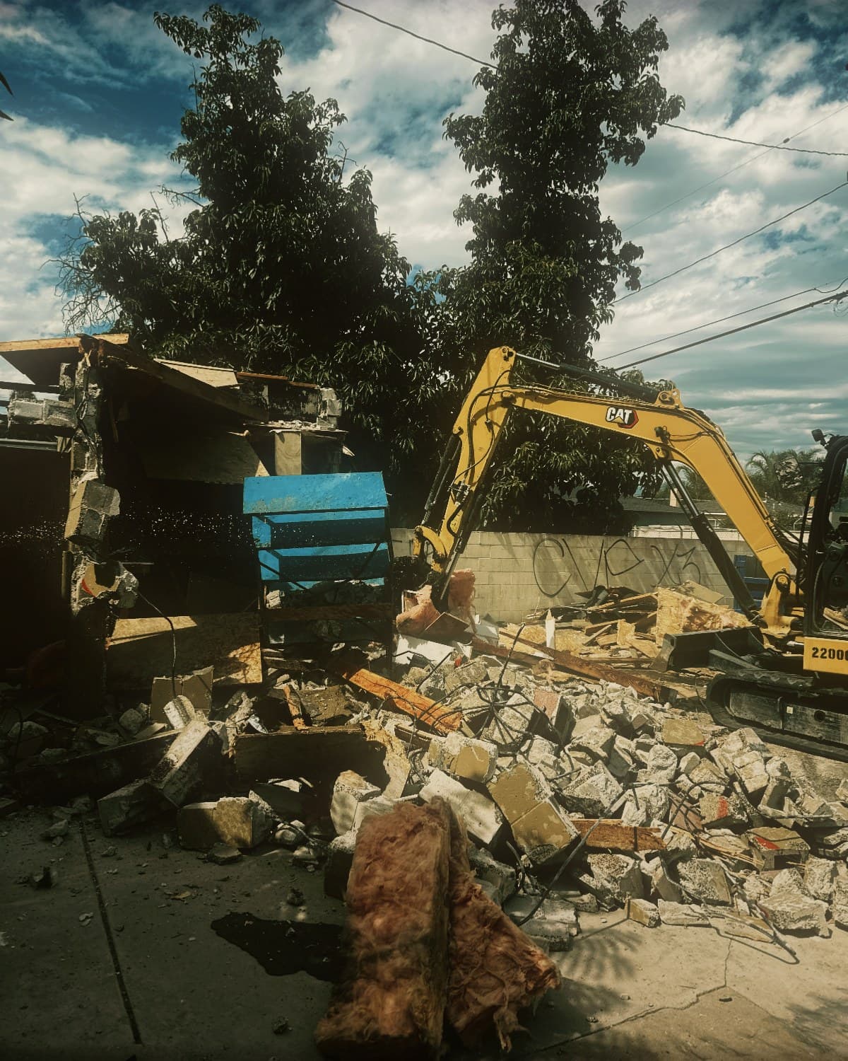 An excavator with a hydraulic breaker demolishing a commercial building wall in Pomona