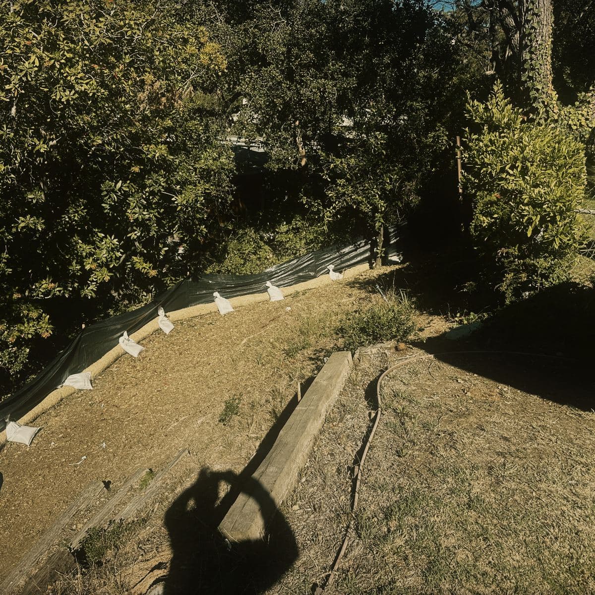 Fiber roll and silt fence pinned along the full length of the site perimeter on the Brentwood hillside, weighted with gravel bags behind a screened construction fence