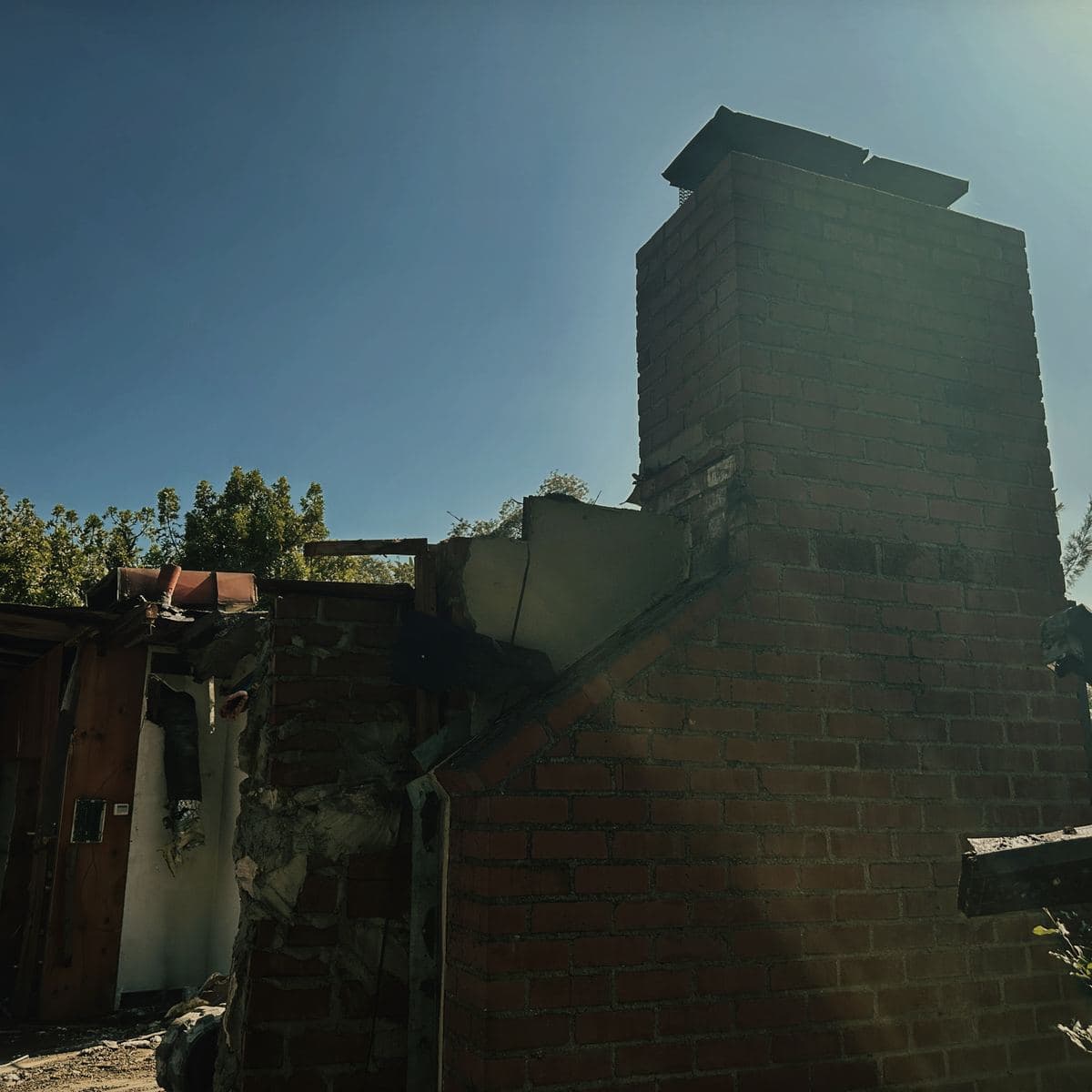 The brick chimney of the demolished house standing alone against the sky on the Brentwood lot, with the rest of the structure already down