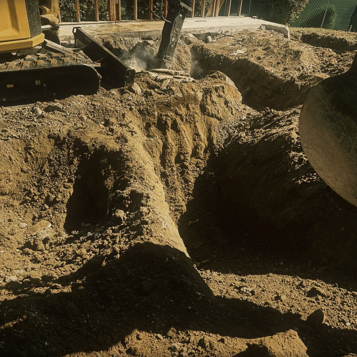 A Caterpillar 305 mini excavator cutting into the rock face of the Brentwood hillside, the bucket in the cut and broken material banked behind it