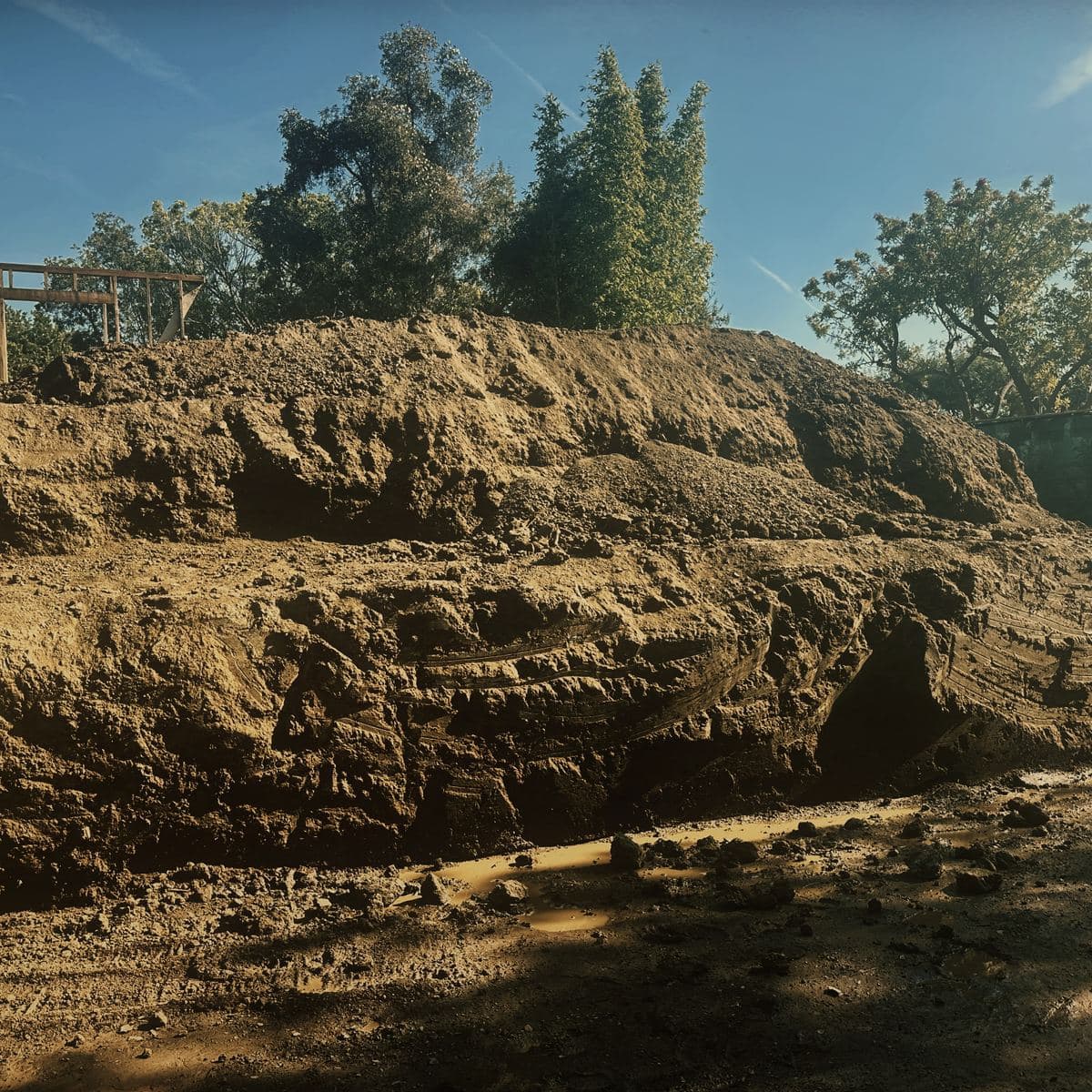 The cut face of the Brentwood hillside excavation standing unsupported above the working platform, its toe lined with sandbags