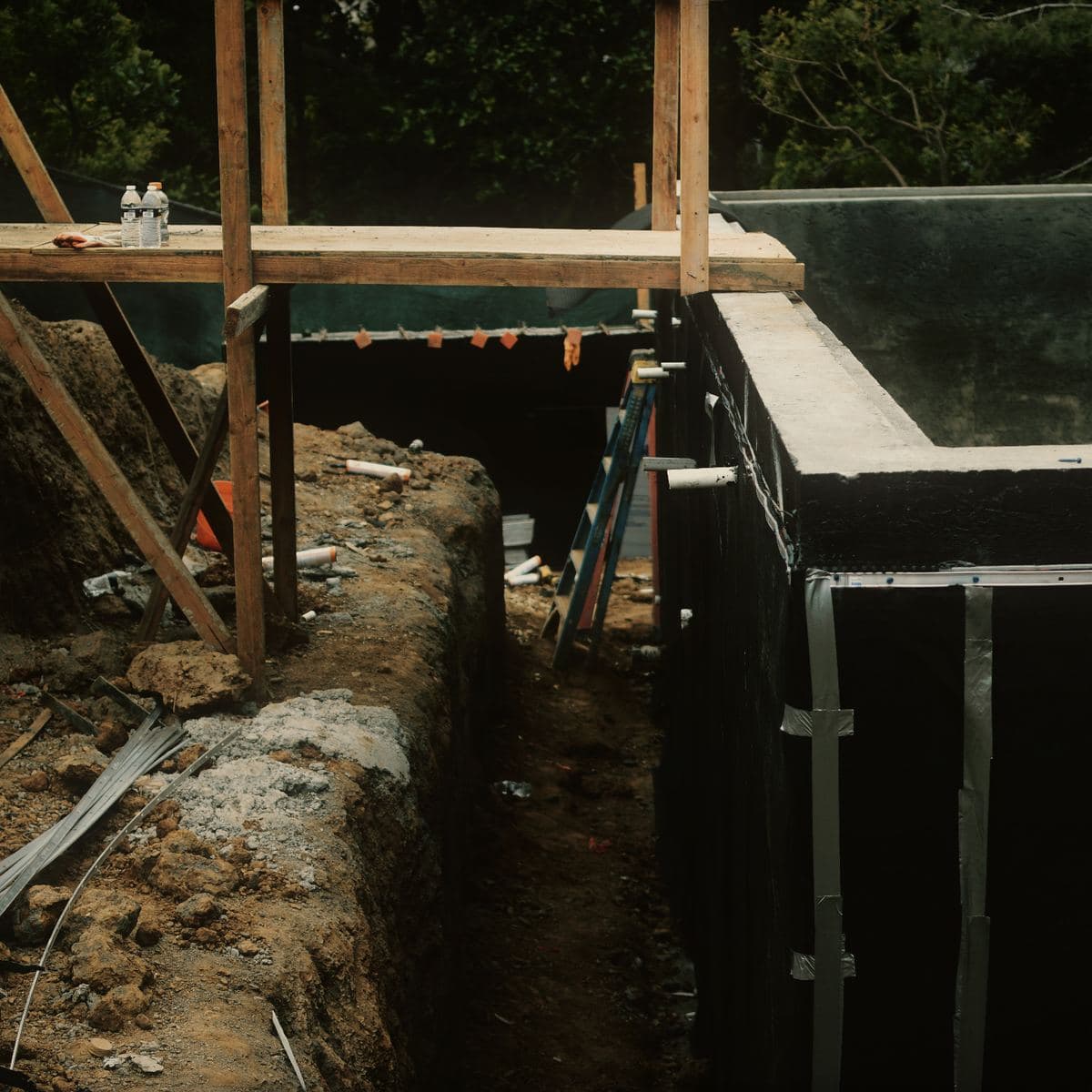 A drainage trench excavated along the outside of the waterproofed Brentwood basement wall, the membrane and its termination bar running the full length above it