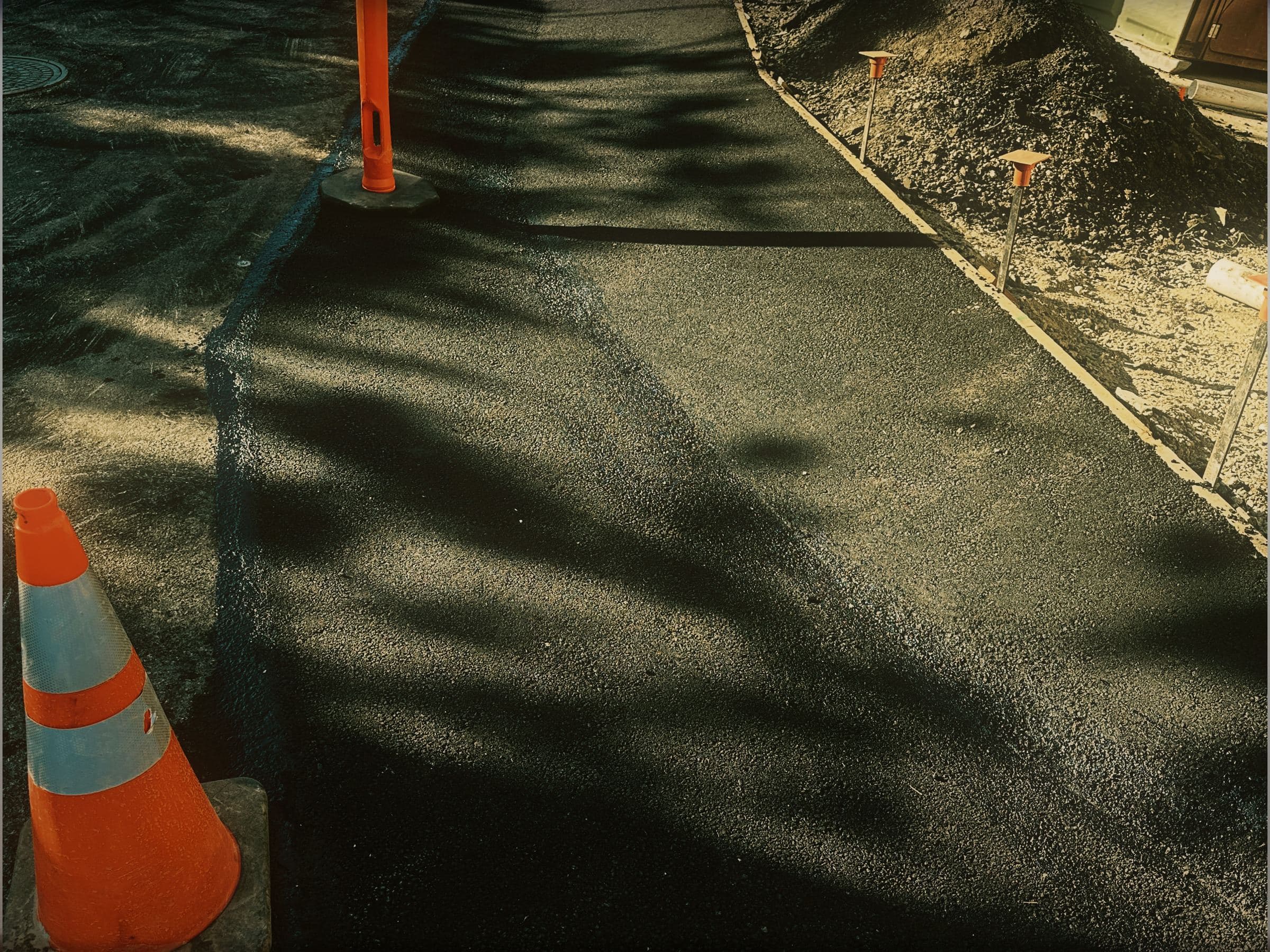 The closed lane on the Brentwood street, cone and delineator taper running up the new asphalt with the formed edge and capped stakes along the far side