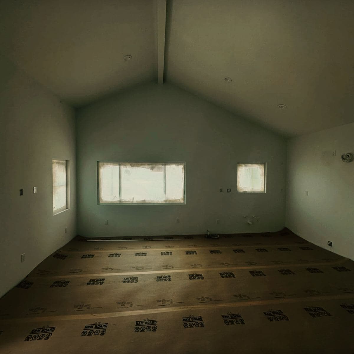 The finished living room of a detached guest house, its vaulted ceiling running to a ridge above three windows, floor protection still down
