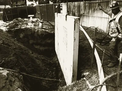 A worker in hard hat and high-visibility vest beside the open trench and pipe run